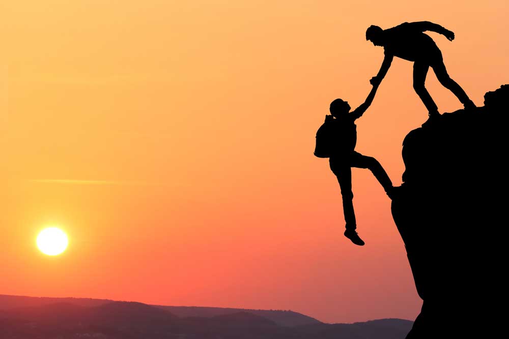 Människa som hjälper en annan människa upp för ett berg i solnedgången