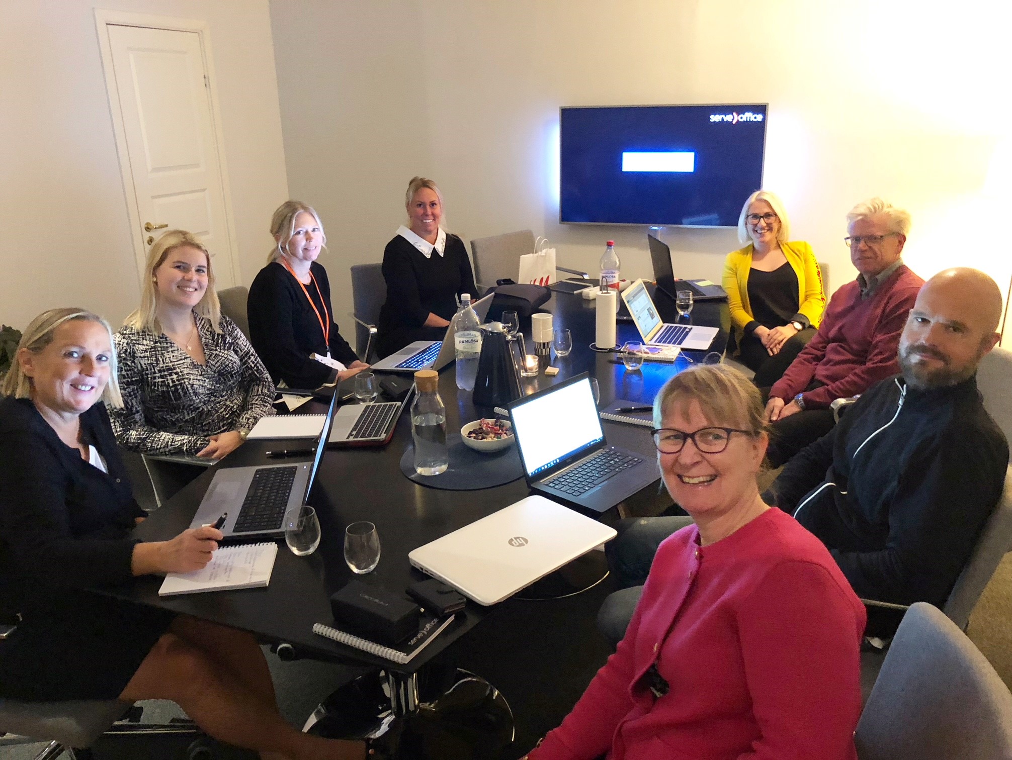 Leende personal på Serveoffice som sitter kring ett bord med laptops