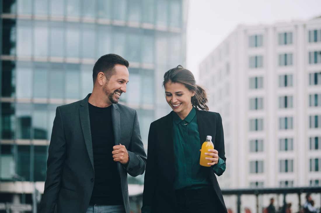 En businesskvinna och en man i kavaj skrattar och går tillsammans